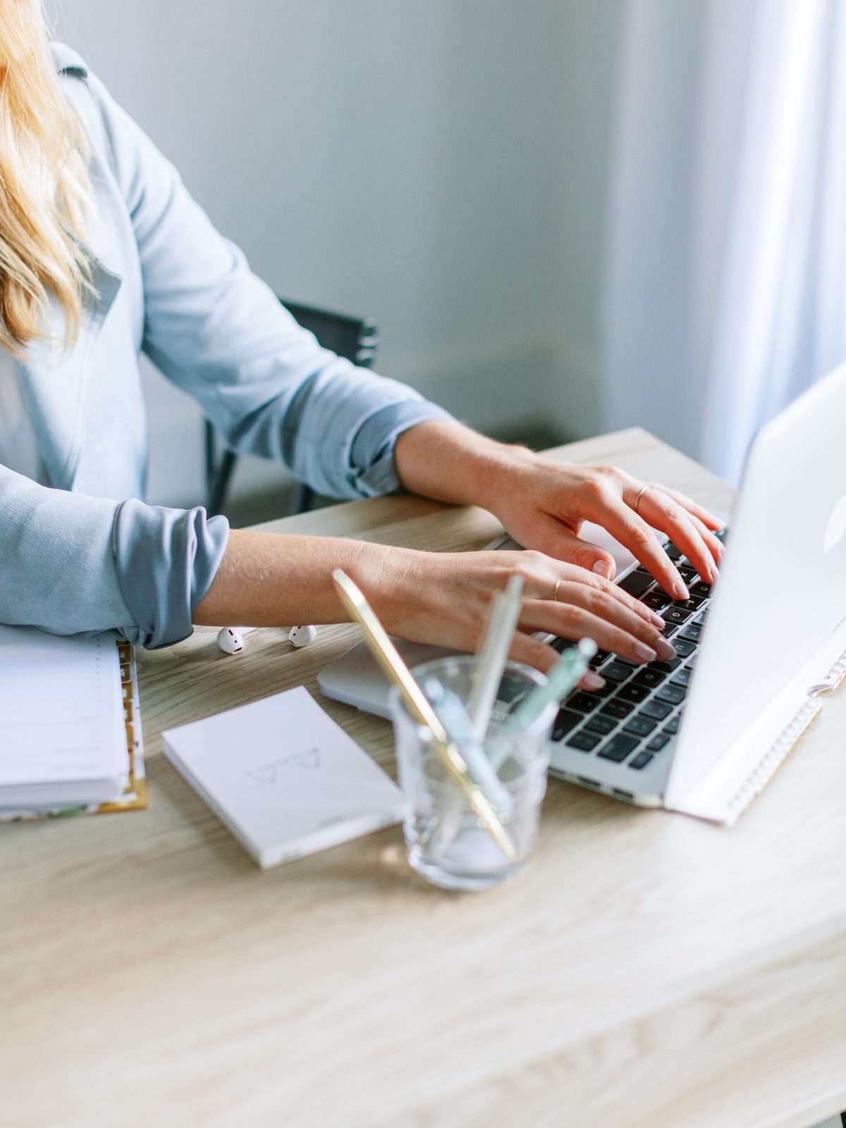 Hands typing on a laptop beside a notebook