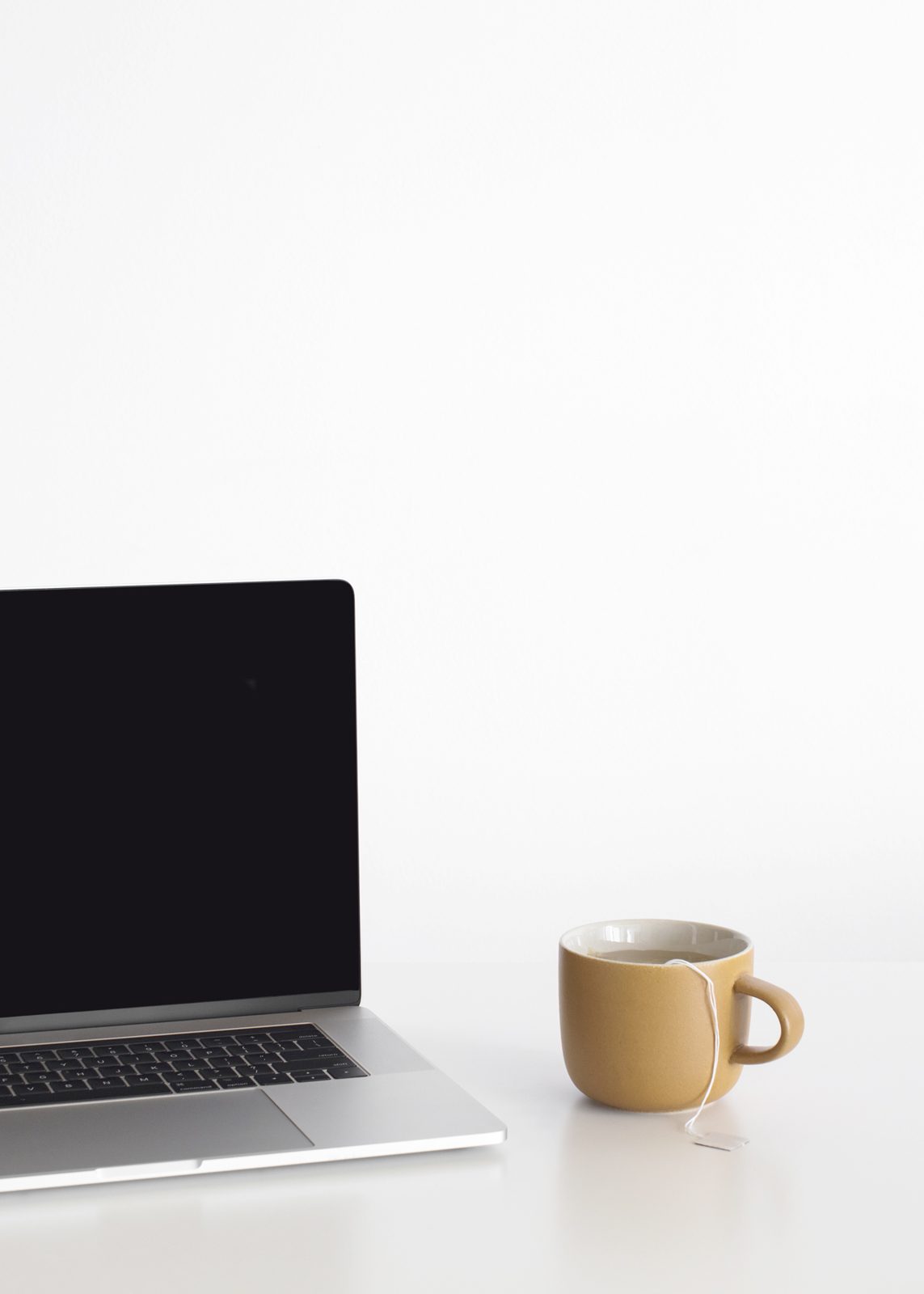 Laptop and a mustard mug on a white desk
